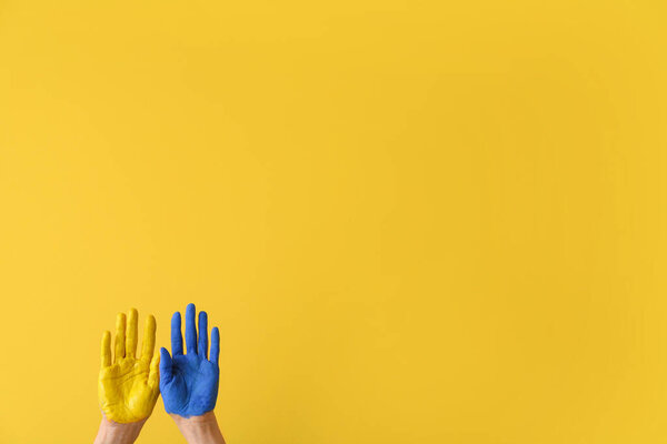 Hands with painted palms in colors of Ukrainian flag on yellow background