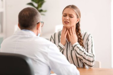 Boğazı ağrıyan bir kadın klinikte doktor ziyareti yapıyor.