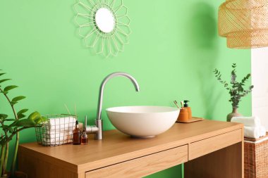 Yeşil duvarın yanında beyaz lavabo ve banyo malzemeleri olan masa.