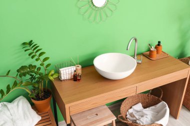 Yeşil duvarın yanında beyaz lavabo ve banyo malzemeleri olan masa.