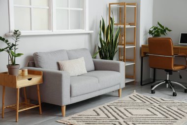 Gri kanepesi ve modern işyeri olan aydınlık oturma odasının içi.