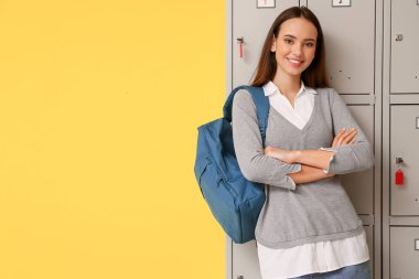 Sarı arka planda dolabın yanındaki kız öğrenci.