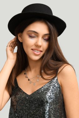 Yaratıcı makyajlı bir kadın açık arkaplanda şık bir şapka giyiyor.