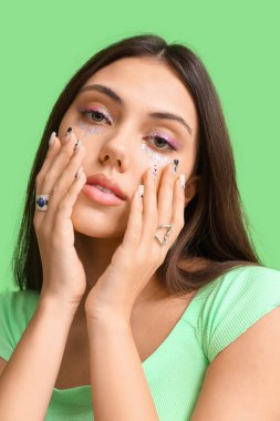 Yaratıcı makyajı ve takıları olan güzel bir kadın yeşil arka plana dokunuyor.