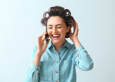 Saç bigudiyle gülen genç bir kadın telefonda konuşuyor.