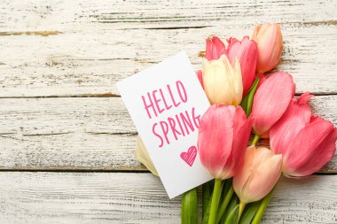 Açık ahşap zemin üzerinde Hello İlkbaharı ve lale çiçekleri buketi içeren kart, yakın plan