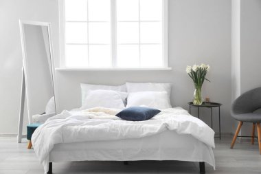 Işıklı yatak odasının içinde vazo ve aynada nergisler var.