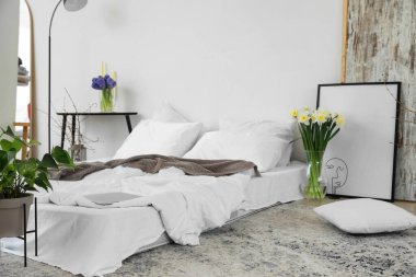 Vazolarda ve çerçevelerde çiçekler olan aydınlık yatak odasının içi