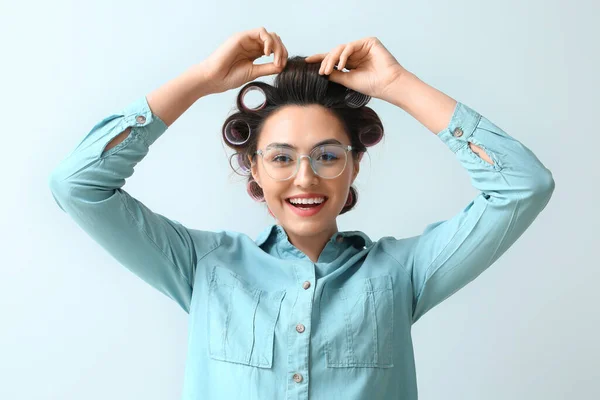 Beautiful young woman in hair rollers on light background