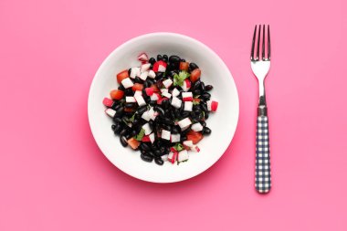 Bir kase lezzetli Meksika salatası, siyah fasulye ve pembe arka planda turp.