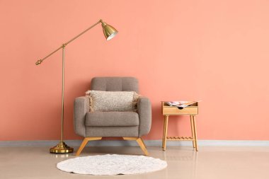 Tahta masa, yumuşak koltuk ve pembe duvarın yanında duran lamba.