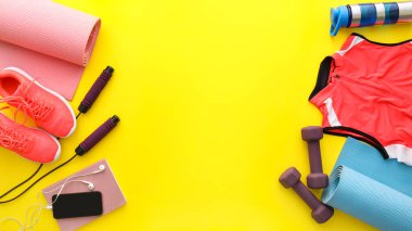 Sarı arka planda farklı spor aletleri, defter ve cep telefonu.