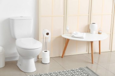 Tuvalet kâsesi, kağıt tutacağı ve banyo malzemeleriyle dolu bir masa.