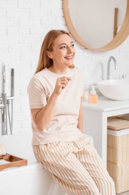 Güzel olgun bir kadın banyoda dişlerini fırçalıyor.