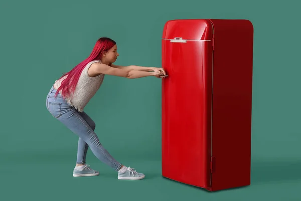 Όμορφη Νεαρή Γυναίκα Προσπαθεί Ανοίξει Κόκκινο Ψυγείο Στο Πράσινο Φόντο — Φωτογραφία Αρχείου