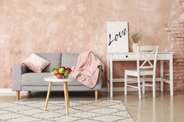 Gri kanepe, işyeri ve meyve sepetli aydınlık oturma odasının içi.