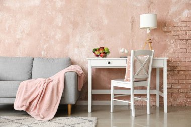 Gri kanepe, işyeri ve meyve sepetli aydınlık oturma odasının içi.