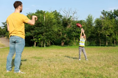 Küçük çocuk babasıyla sahada rugby oynuyor.