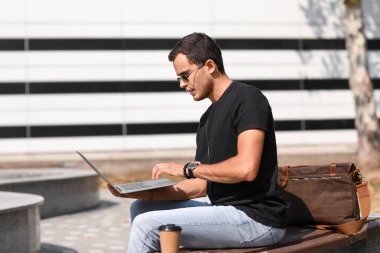 Dışarıda dizüstü bilgisayar kullanan yakışıklı bir adam.
