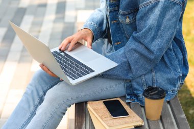 Genç adam parktaki bankta dizüstü bilgisayar kullanıyor.