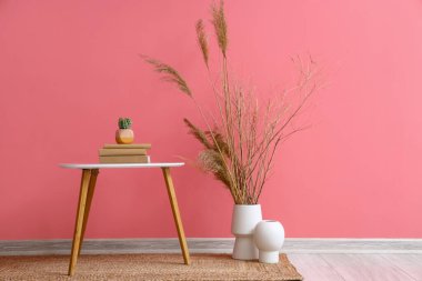 Pembe duvarın yanında kitap ve vazolarla dolu bir masa.