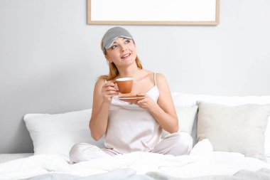 Yetişkin bir kadının yatakta kahve içtiği bir sabah.