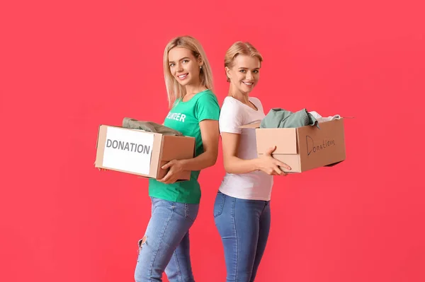 Young women holding boxes with clothes for donation on red background