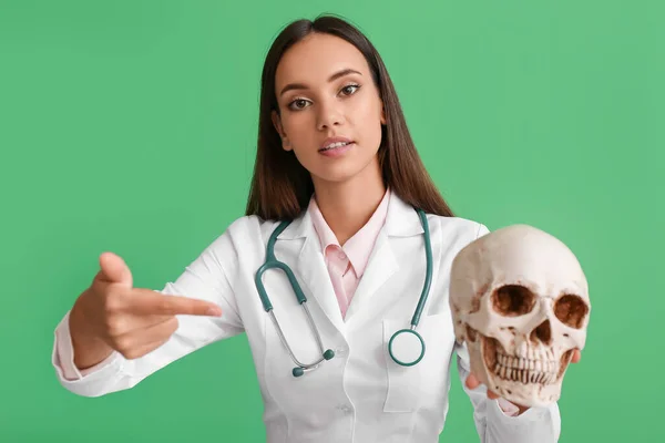 Female doctor with human skull on color background