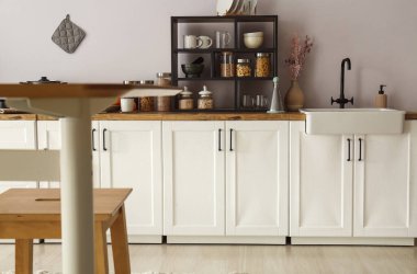 Mutfak duvarının yanında raflı, lavabolu ve yiyecekli beyaz tezgahlar.