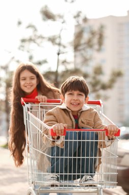 Dışarıda alışveriş arabasıyla oynayan sevimli çocuklar.