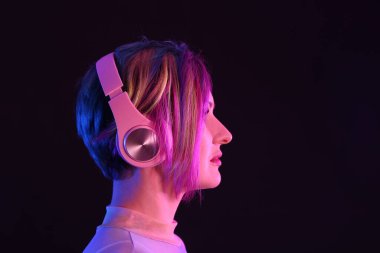 Sıradışı saçlı güzel bir kadın siyah arka planda müzik dinliyor.