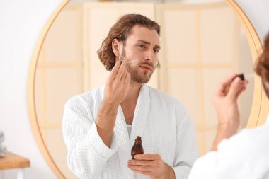 Genç adam banyoda cilt bakımı için serum kullanıyor.
