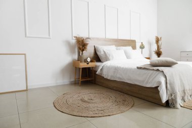 Rahat yatak, hasır halı ve beyaz duvarın yanında kuru kamışlı komodin masası.