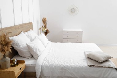 Rahat yatak, kuru sazlıklar ve beyaz duvarın yanındaki çekmeceler.