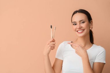 Bej arka plandaki diş fırçalarını gösteren genç bir kadın.