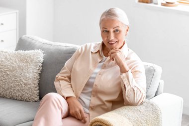 Olgun bir kadın evdeki yumuşak koltukta oturuyor.