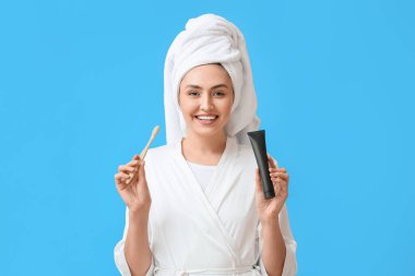 Bornozlu, aktif kömür diş macunu ve mavi arka planda fırçası olan güzel bir kadın.