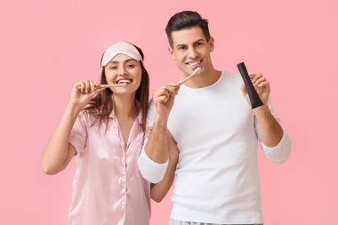 Pembe arka planda aktif kömür diş macunu kullanan genç bir çift.