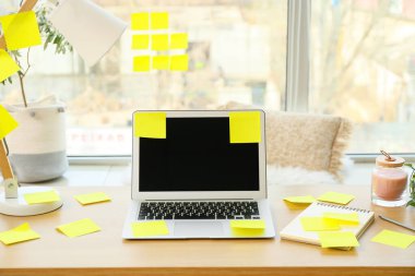 Pencerenin yanındaki masada not defteri ve yapışkan notları olan bir dizüstü bilgisayar.