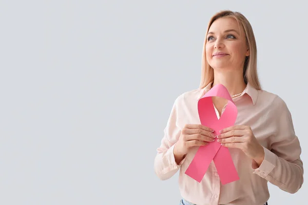 Woman holding pink awareness ribbon and looking aside on light background. Breast cancer awareness concept