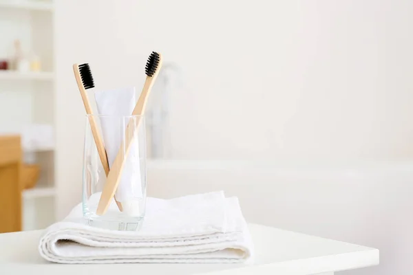 Holder with toothbrushes, towel and toothpaste on table in bathroom
