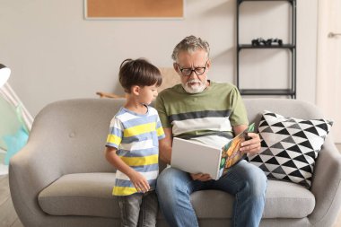 Son sınıf öğrencisi, evdeki kanepede torununa masal okuyor.