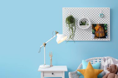 Çocuk odasındaki mavi duvarda ev bitkileri ve kitap asılı Peg tahtası.