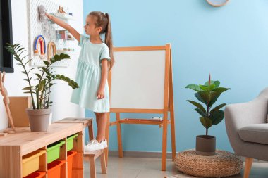 Sevimli küçük kız oyuncaklarını duvarda asılı duran tahta tahtadan alıyor.