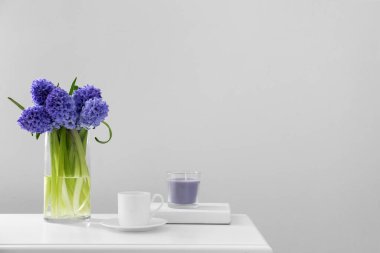 Vazo, sümbül çiçekleri, bardak ve mum ışık duvarının yanındaki masada.