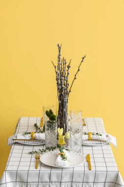 Vase with pussy willow branches on table served for Easter celebration near yellow wall