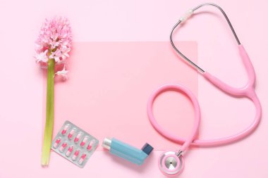 İçinde boş kağıt, astım spreyi, haplar, steteskop ve pembe arka planda sümbül çiçeği olan kompozisyon