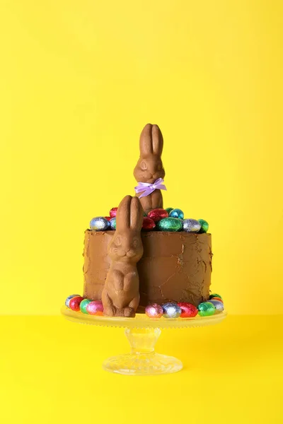 黄色の背景にチョコレートバニーと卵で飾られたおいしいイースターケーキ — ストック写真