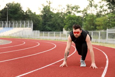 Güneş gözlüklü genç adam stadyumda koşmaya hazırlanıyor.