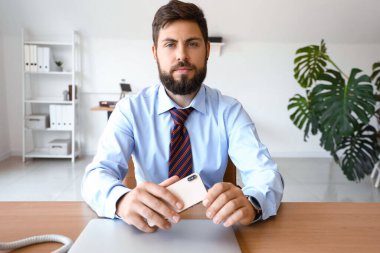 Ofisinde cep telefonu olan yakışıklı genç bir iş adamı.